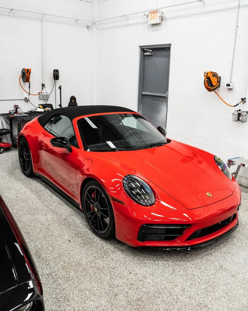 Red Porsche convertible parked inside a detailing shop with paint protection film applied.